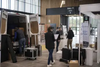 B2B exhibitors unloading stand materials from a van inside Parc Expo Rennes during a calm early morning setup, with natural daylight and casual interaction.