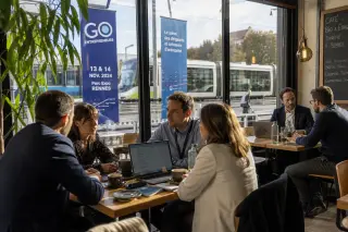 Lively café in Rennes with locals and visitors engaged in discreet discussion, event banners visible outside, natural daylight, documentary style.