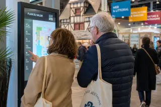 Visitors quietly discussing a digital map inside a lively thematic pavilion at Rennes Exhibition Centre, with subtle Breton decor and soft daylight.