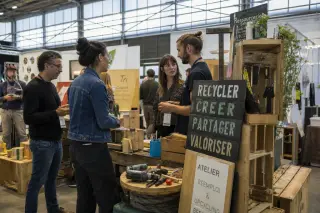 Exhibitors collaborating around reused materials at the Parc des Expositions de Rennes, with upcycled displays and natural daylight accentuating authentic activity.